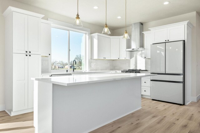 kitchen with white cabinets, freestanding refrigerator, recessed lighting, light wood-style floors, and wall chimney range hood