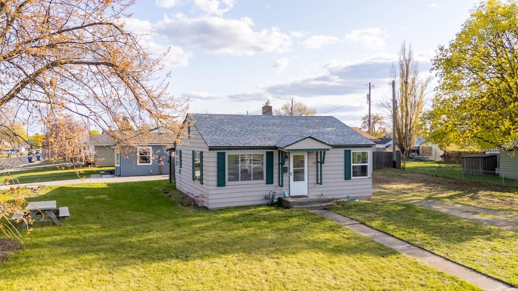 bungalow-style house with fence, a shingled roof, a chimney, and a front yard