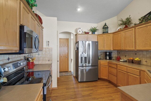 kitchen featuring arched walkways, light wood-type flooring, decorative backsplash, light countertops, and appliances with stainless steel finishes