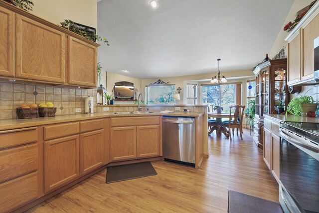 kitchen featuring light wood finished floors, an inviting chandelier, a sink, a peninsula, and appliances with stainless steel finishes