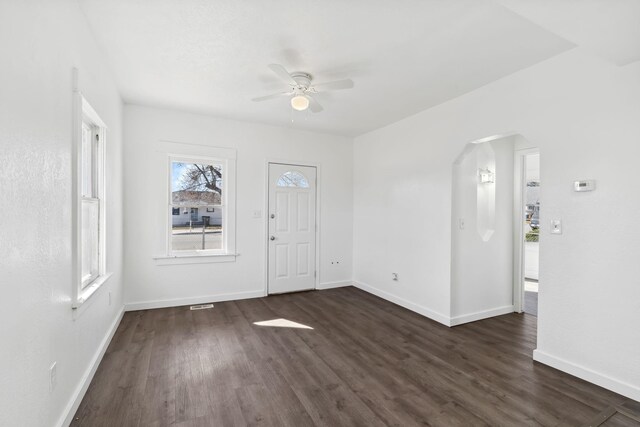 entryway featuring a ceiling fan, baseboards, arched walkways, and dark wood-type flooring