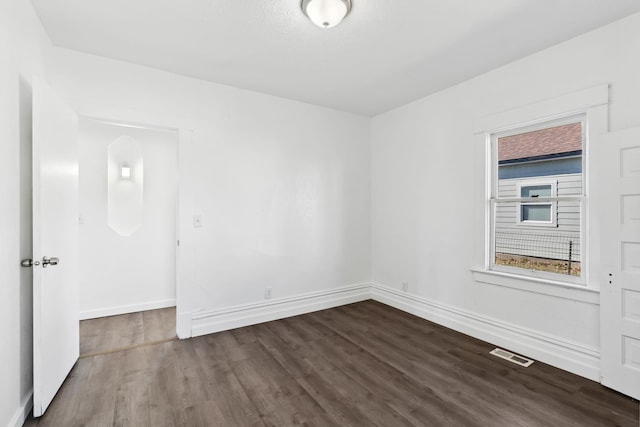 spare room featuring dark wood-type flooring, visible vents, and baseboards