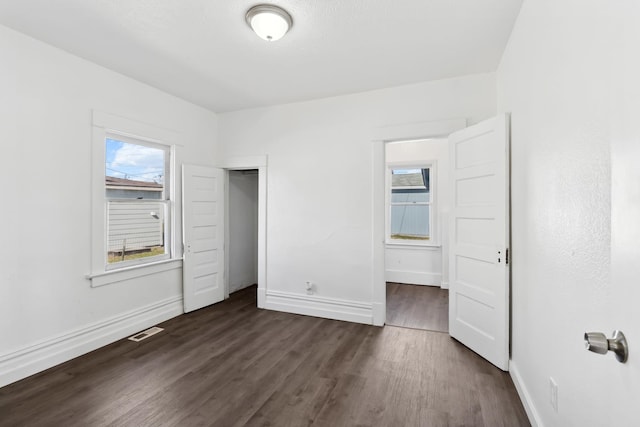 unfurnished bedroom with dark wood finished floors, baseboards, visible vents, and a closet