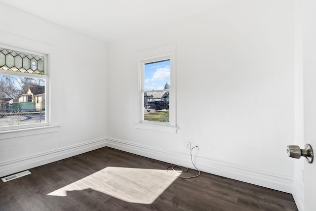 spare room featuring plenty of natural light, baseboards, visible vents, and dark wood finished floors