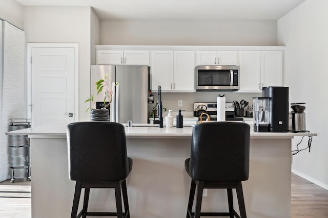 18706 E Flat Rock River Ave, Spokane Valley, WA 99016 - kitchen with a kitchen breakfast bar, a center island with sink, white cabinetry, wood finished floors, and appliances with stainless steel finishes