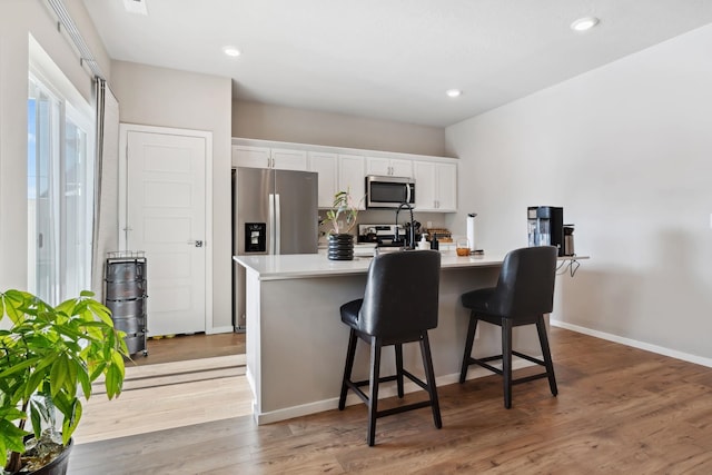 18706 E Flat Rock River Ave, Spokane Valley, WA 99016 - kitchen featuring white cabinets, light wood finished floors, a center island with sink, light countertops, and appliances with stainless steel finishes
