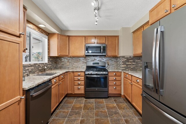 kitchen featuring light stone counters, a sink, a textured ceiling, decorative backsplash, and appliances with stainless steel finishes