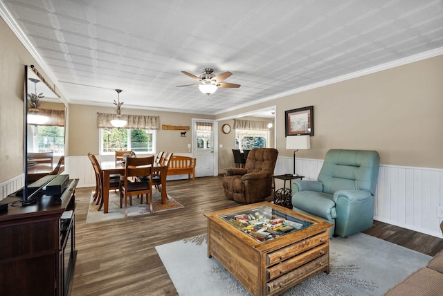living room with crown molding, a wainscoted wall, dark wood-style floors, and a ceiling fan