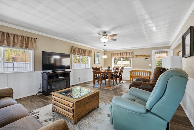 living area with ceiling fan, a healthy amount of sunlight, a wainscoted wall, and wood finished floors