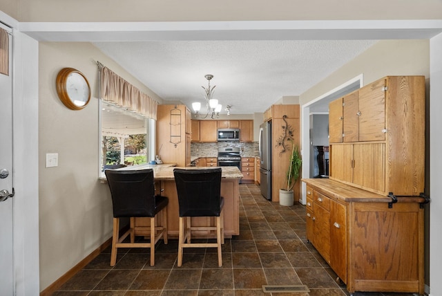 kitchen with a peninsula, an inviting chandelier, decorative backsplash, light countertops, and appliances with stainless steel finishes