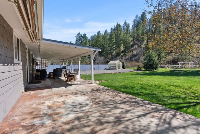 view of patio featuring an outdoor structure, fence, a carport, and driveway