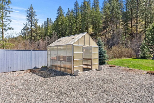 view of greenhouse with a yard and fence