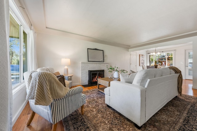 living room featuring baseboards, a brick fireplace, wood finished floors, and an inviting chandelier