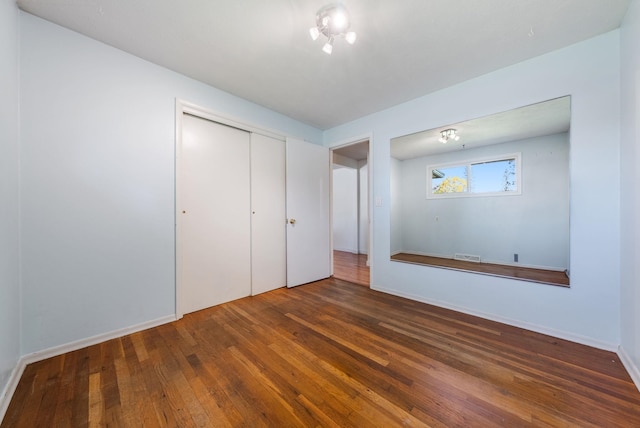 unfurnished bedroom with wood-type flooring, a closet, baseboards, and visible vents