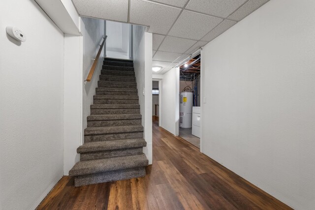 staircase with a paneled ceiling, wood finished floors, and water heater