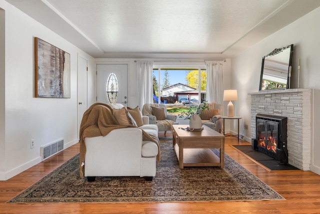 living area featuring a fireplace, a raised ceiling, wood finished floors, and visible vents
