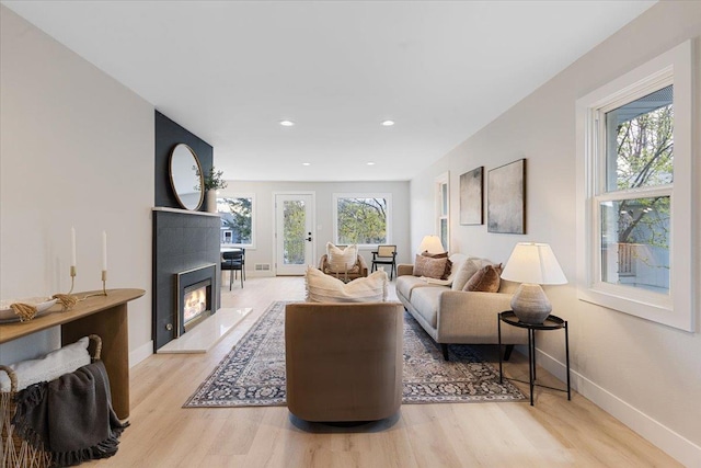 living area with baseboards, a glass covered fireplace, and light wood-type flooring