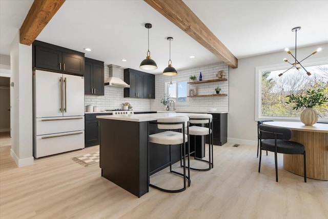 kitchen with high end white fridge, light wood finished floors, wall chimney exhaust hood, backsplash, and baseboards