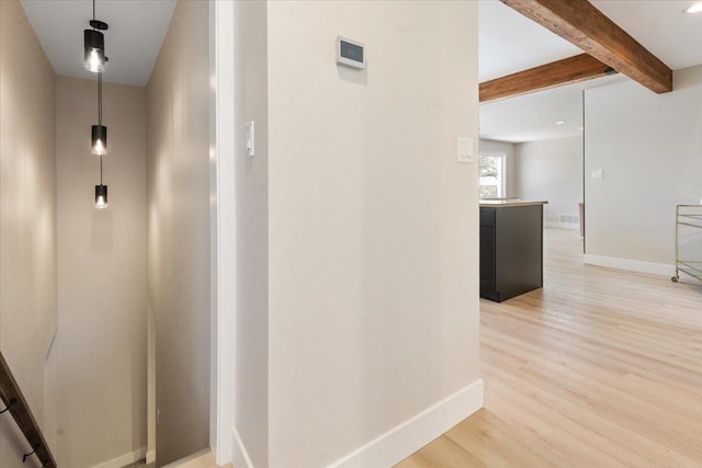 hall with light wood-style flooring, baseboards, beam ceiling, and an upstairs landing