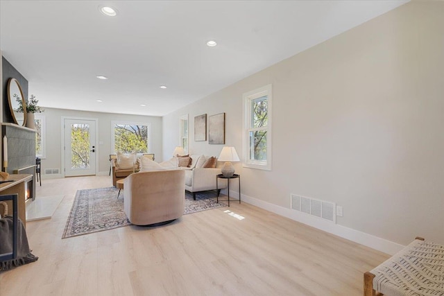 living room with baseboards, light wood-style flooring, visible vents, and a wealth of natural light
