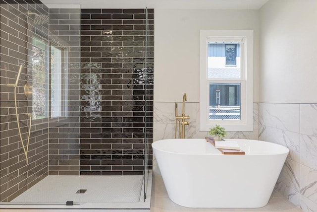 bathroom with a freestanding bath, tile walls, tiled shower, and wainscoting