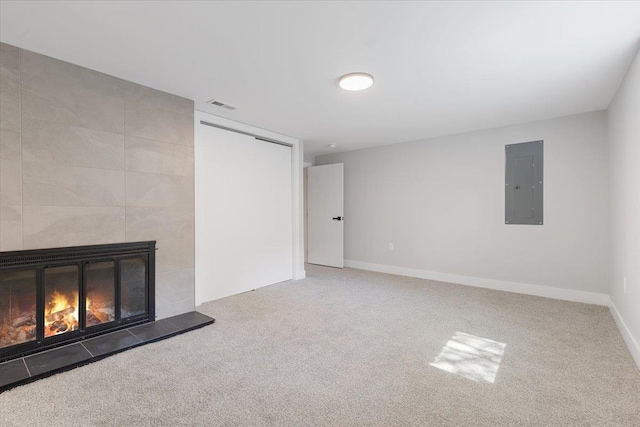 unfurnished living room with visible vents, electric panel, baseboards, a tiled fireplace, and carpet flooring