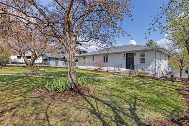 rear view of house with a lawn, a chimney, and brick siding