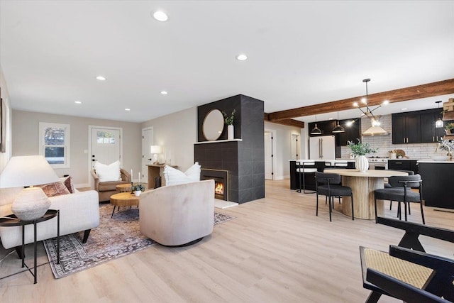 living area with recessed lighting, light wood-style flooring, beam ceiling, and a large fireplace