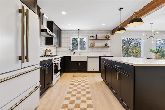 kitchen featuring light countertops, wall chimney range hood, a sink, white appliances, and tasteful backsplash