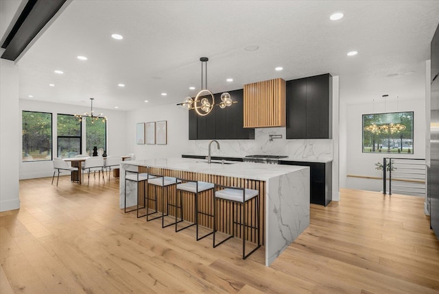27603 N Bruce Rd, Chattaroy, WA 99003 - kitchen with dark cabinetry, a sink, decorative backsplash, a chandelier, and light wood-style flooring