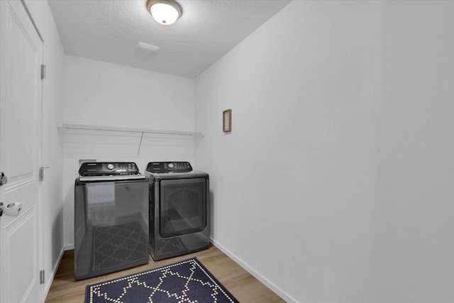 laundry room featuring a textured ceiling, light wood-type flooring, washer and dryer, baseboards, and laundry area
