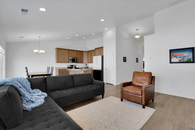living area with light wood finished floors, vaulted ceiling, visible vents, and an inviting chandelier