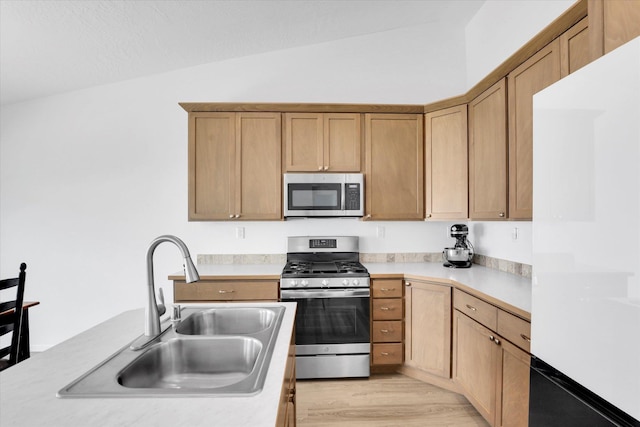 kitchen featuring light wood finished floors, light countertops, vaulted ceiling, a sink, and appliances with stainless steel finishes