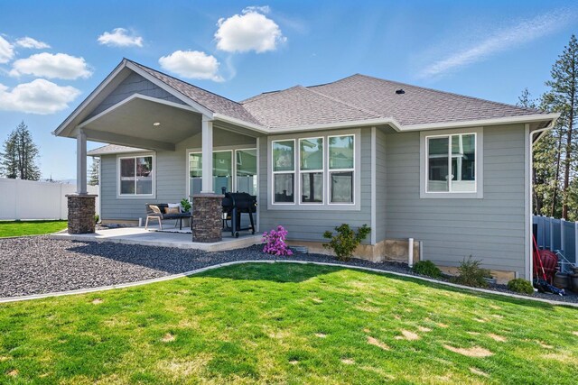 rear view of property with a patio area, roof with shingles, fence, and a yard