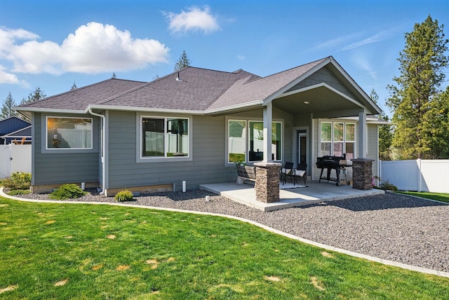 rear view of house with fence, a shingled roof, a yard, and a patio