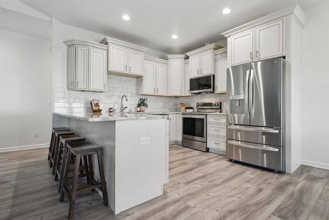 kitchen with light wood-type flooring, baseboards, a kitchen bar, and appliances with stainless steel finishes