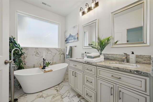 bathroom with marble finish floor, a freestanding bath, double vanity, visible vents, and a sink