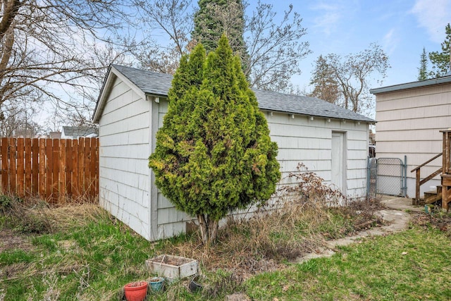 exterior space featuring fence, an outdoor structure, and roof with shingles