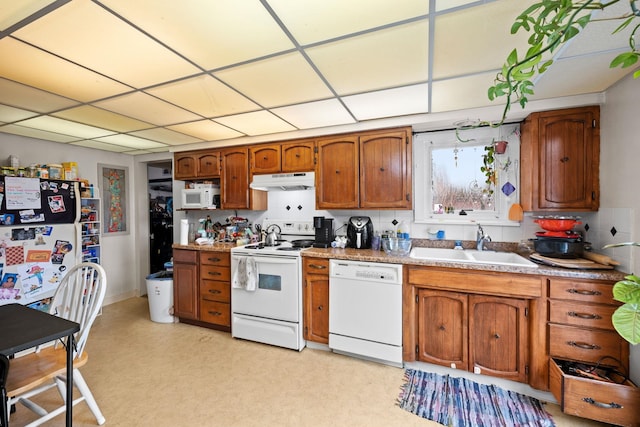 kitchen featuring brown cabinetry, white appliances, a paneled ceiling, under cabinet range hood, and a sink