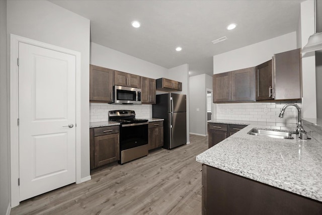 kitchen with decorative backsplash, a sink, appliances with stainless steel finishes, dark brown cabinetry, and light stone countertops
