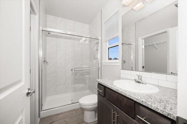 bathroom featuring wood finished floors, a shower stall, toilet, and vanity