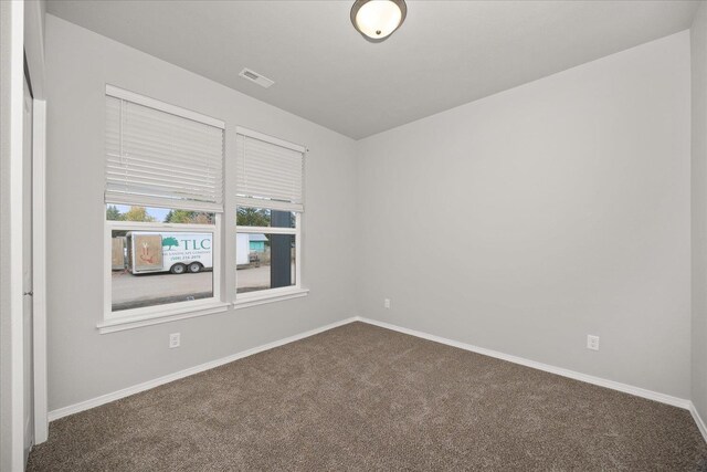 spare room with visible vents, dark colored carpet, and baseboards