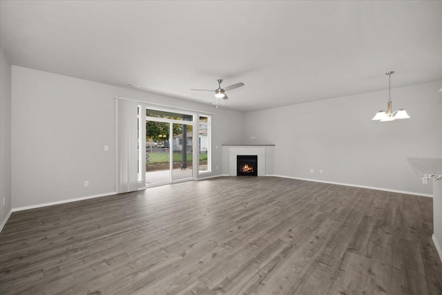 unfurnished living room featuring baseboards, wood finished floors, ceiling fan with notable chandelier, and a fireplace