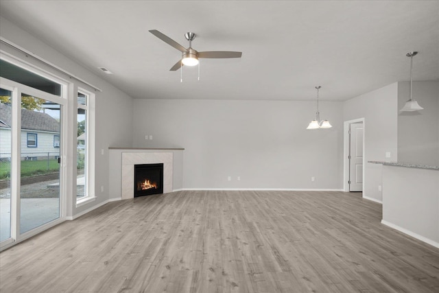 unfurnished living room featuring light wood-type flooring, baseboards, a high end fireplace, and ceiling fan with notable chandelier