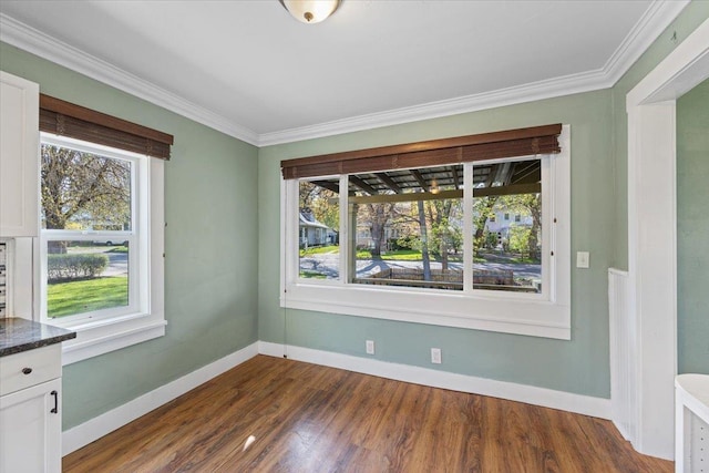 unfurnished dining area with dark wood-type flooring, crown molding, and baseboards