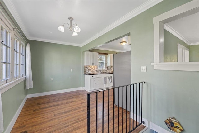 corridor featuring crown molding, dark wood-style floors, a notable chandelier, and baseboards