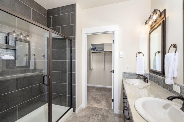 bathroom featuring double vanity, a walk in closet, a stall shower, and a sink