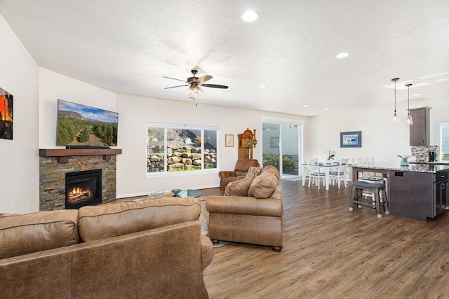 living area featuring a healthy amount of sunlight, wood finished floors, a ceiling fan, and a stone fireplace