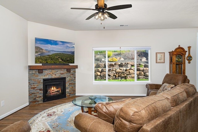 living room with a fireplace, a ceiling fan, visible vents, baseboards, and wood finished floors