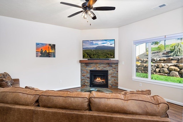 living room with a fireplace, a ceiling fan, visible vents, baseboards, and wood finished floors